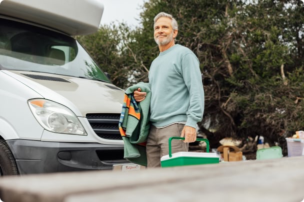 man holding cooler and blanket next to camper