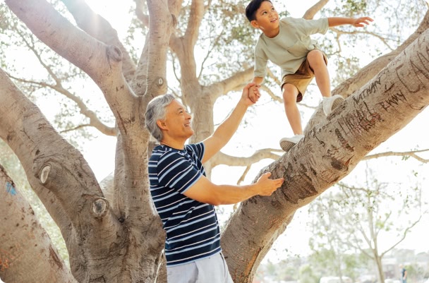 man helping a little boy climb a tree